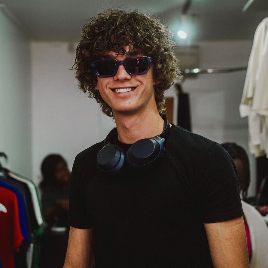 Man wearing sunglasses and a black shirt with headphones around his neck in a clothing store.